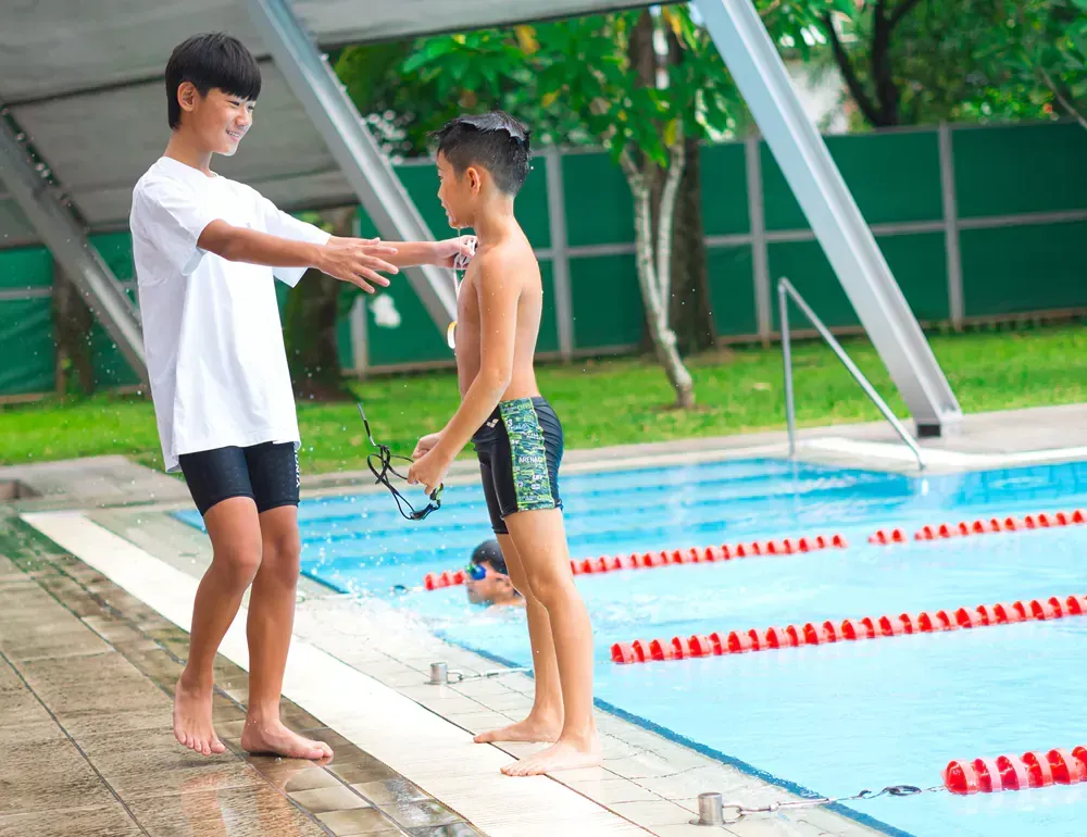 Two young boys are standing next to a swimming pool.