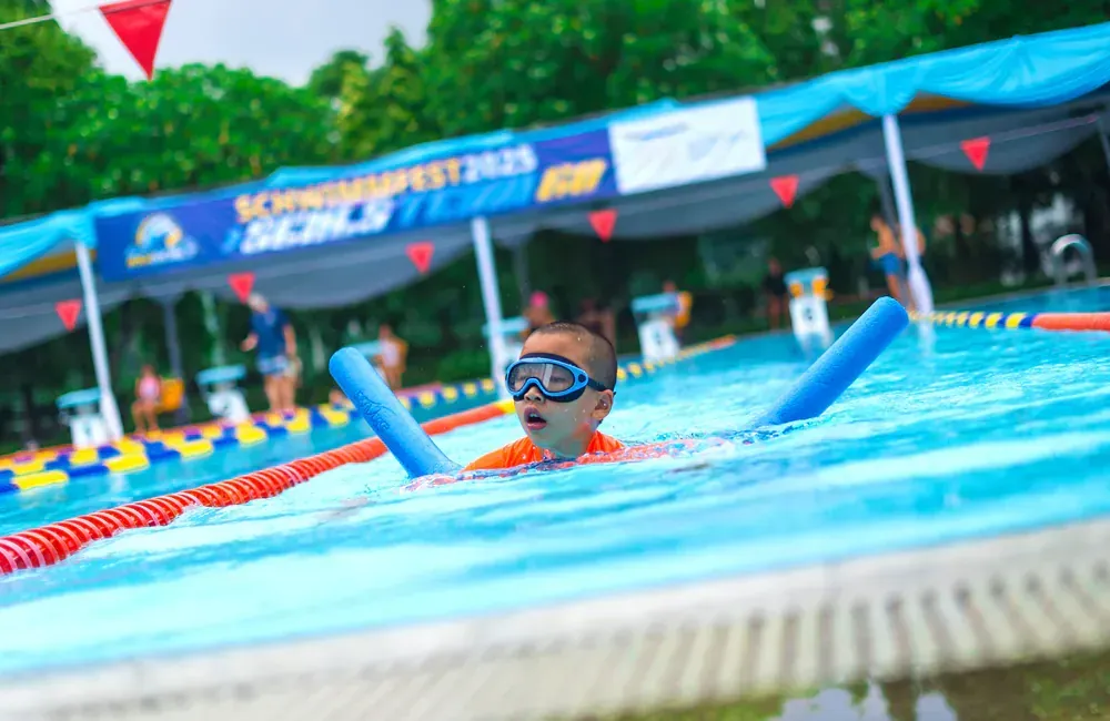 A young boy is swimming in a swimming pool with foam noodles.