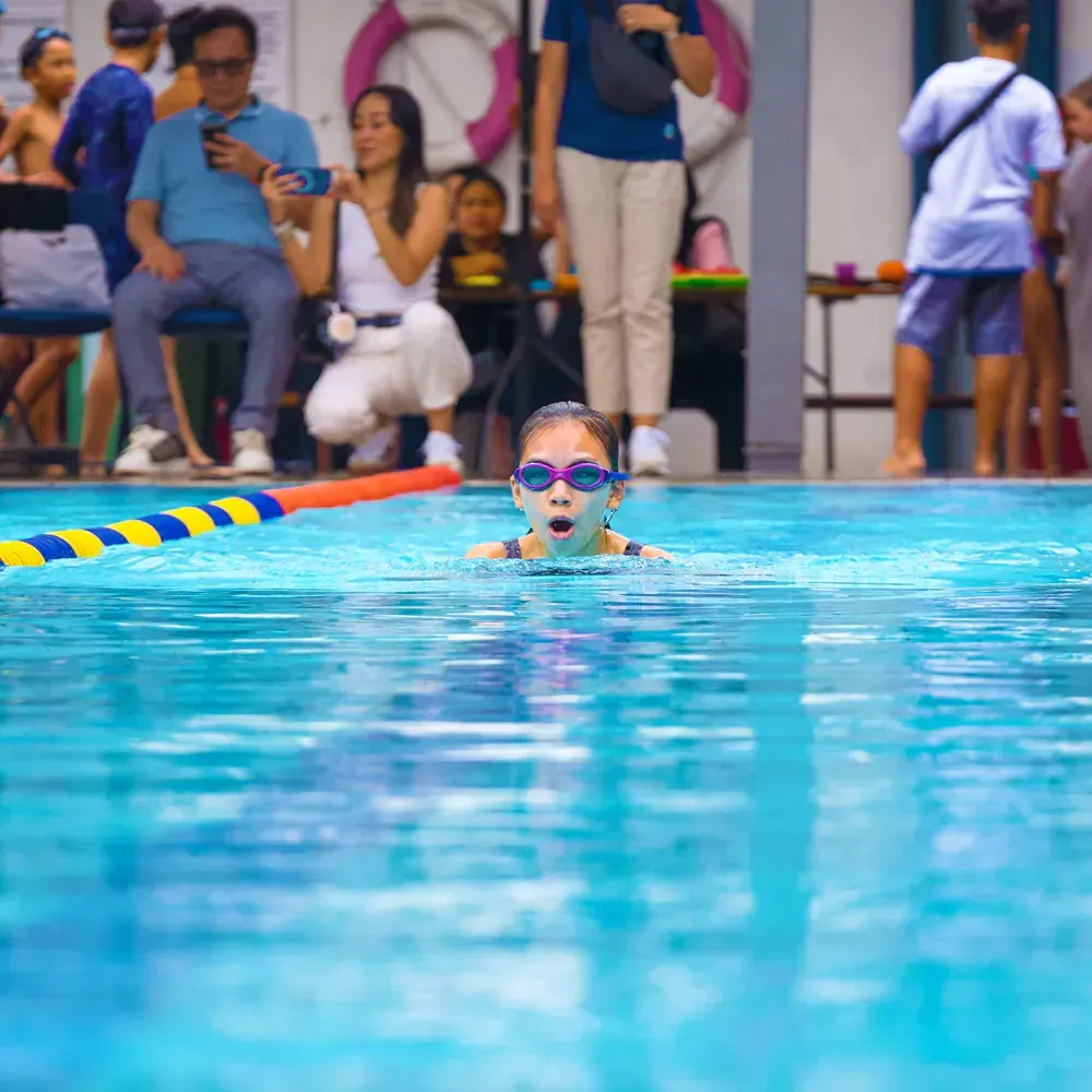 A young girl wearing goggles is swimming in a swimming pool.