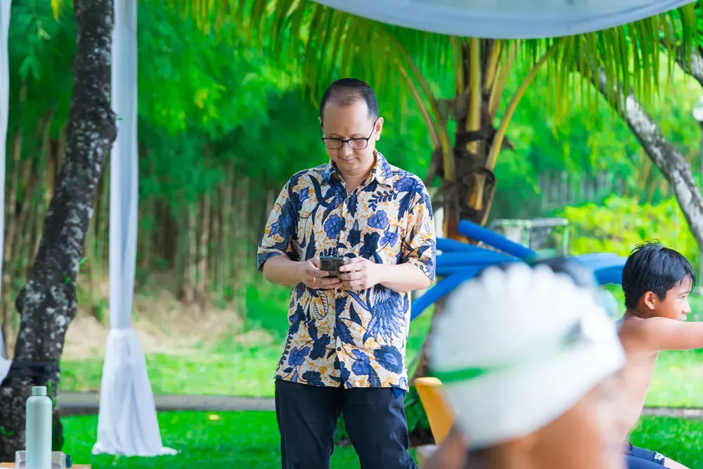 A man is standing in a park looking at his cell phone.