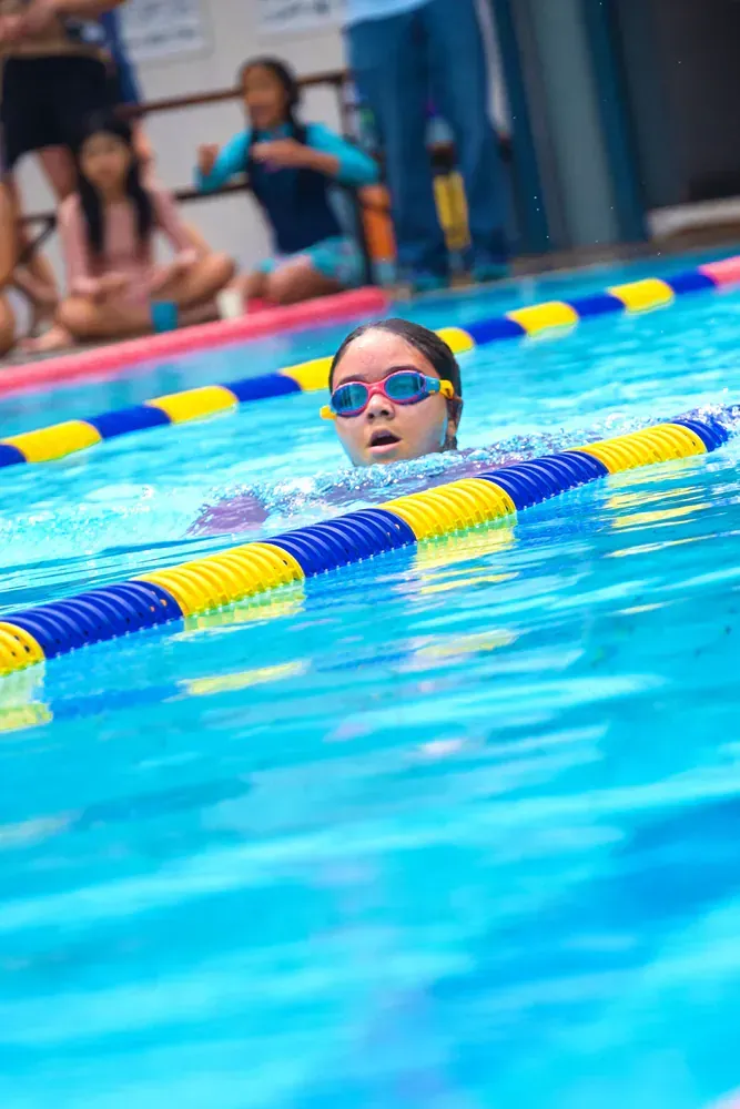 A young girl wearing goggles is swimming in a swimming pool.