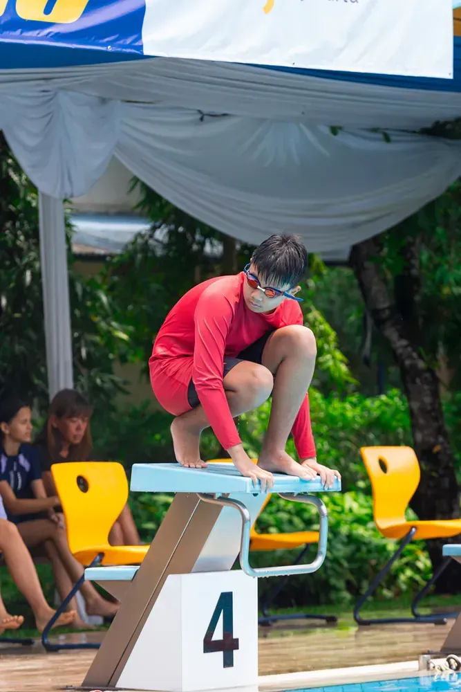 A boy is squatting on a diving board with the number 4 on it