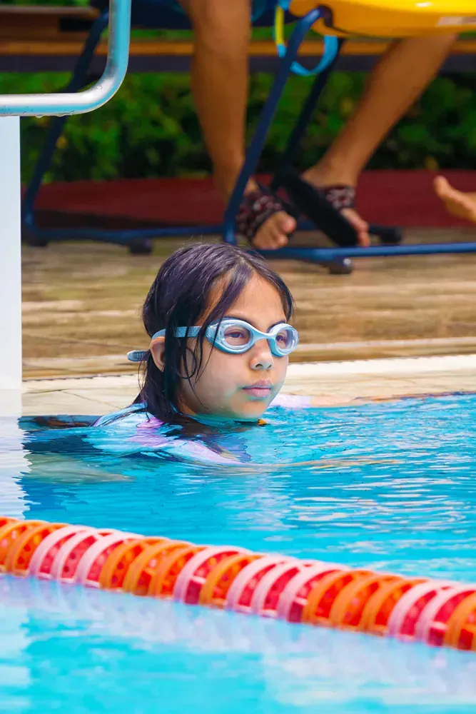 A young girl wearing goggles is swimming in a swimming pool.