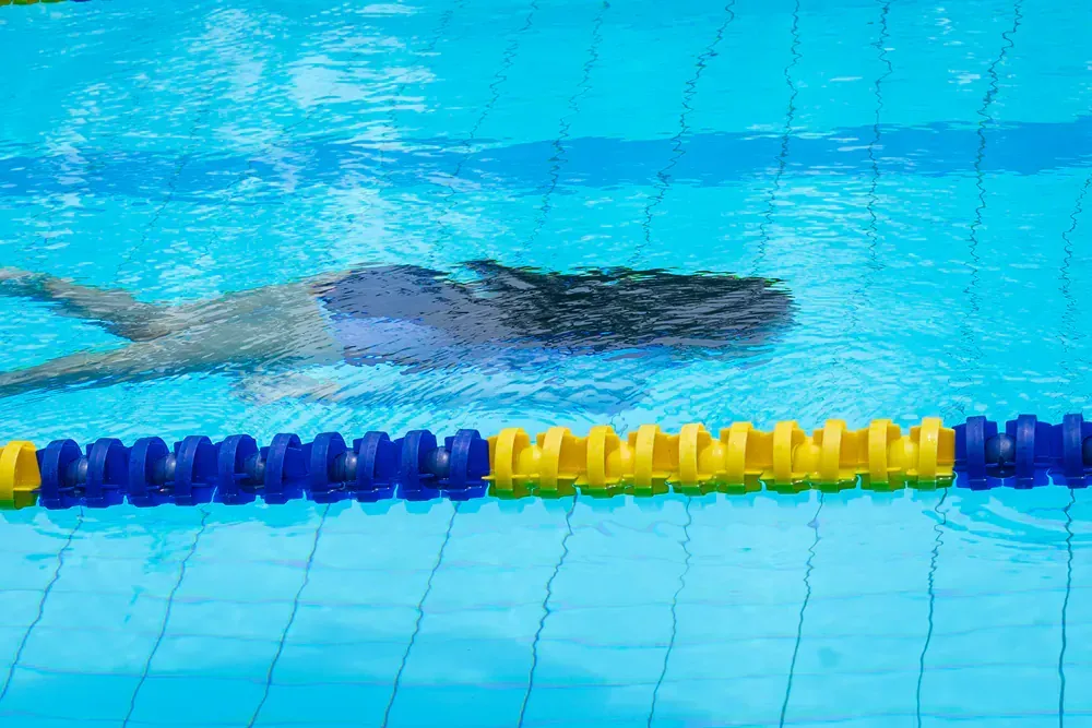 A person is swimming in a swimming pool with a yellow and blue lane.