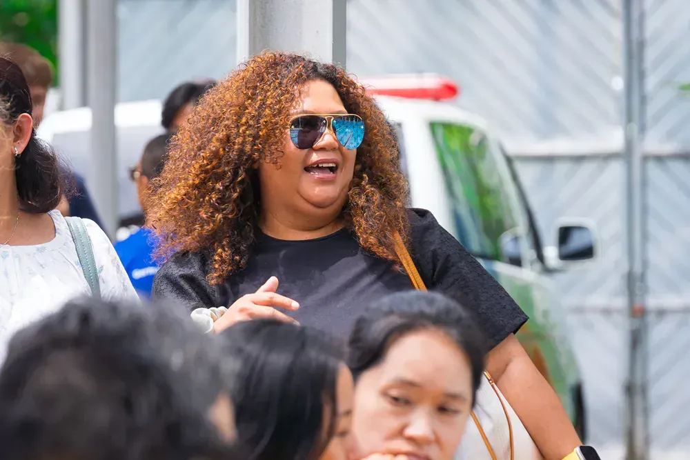 A woman wearing sunglasses is standing in a crowd of people.