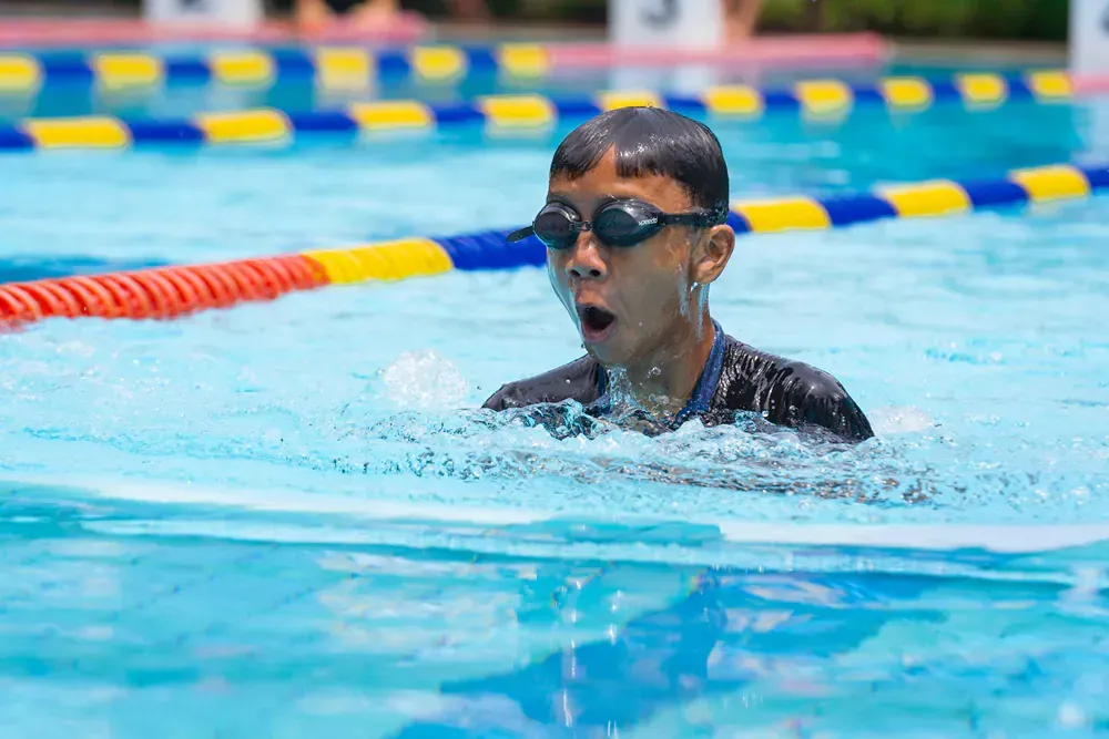 A young boy wearing goggles is swimming in a swimming pool.