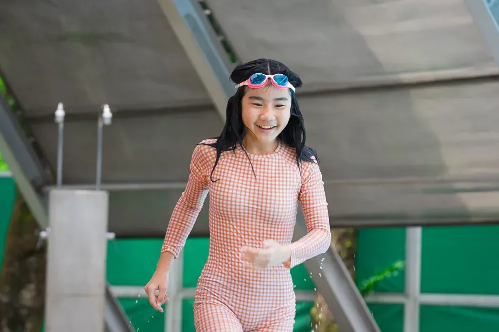 A young girl in a swimsuit and goggles is running in a pool.