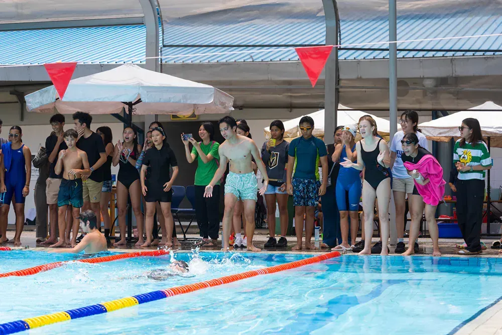 A group of people are standing around a swimming pool watching a swimmer.