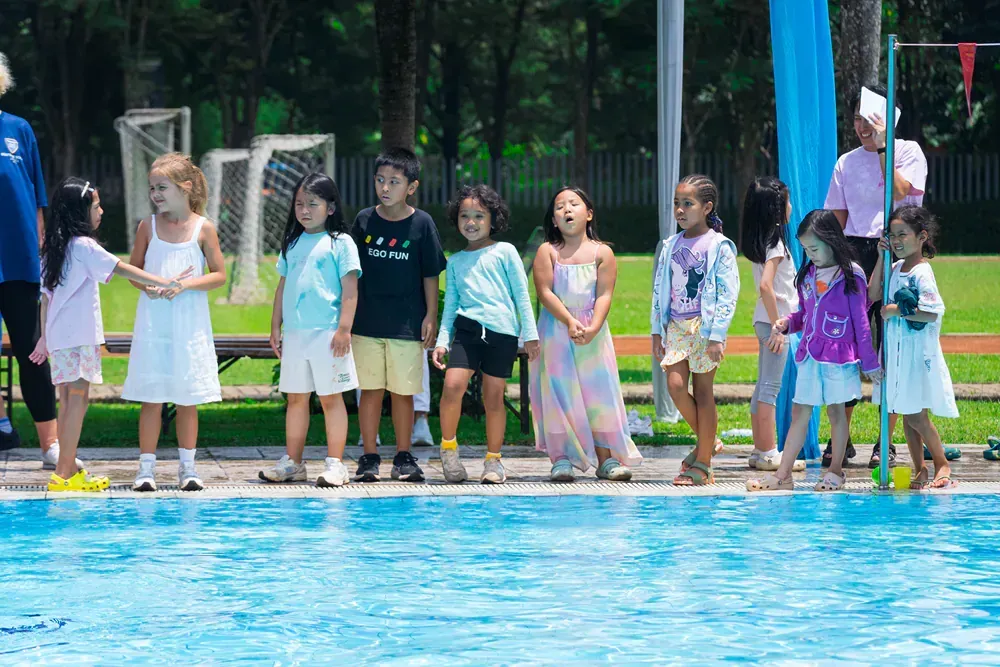 A group of children are standing next to a swimming pool.
