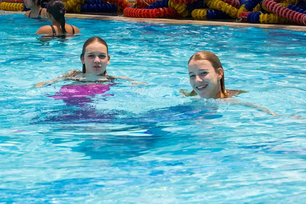 Two young girls are swimming in a swimming pool.