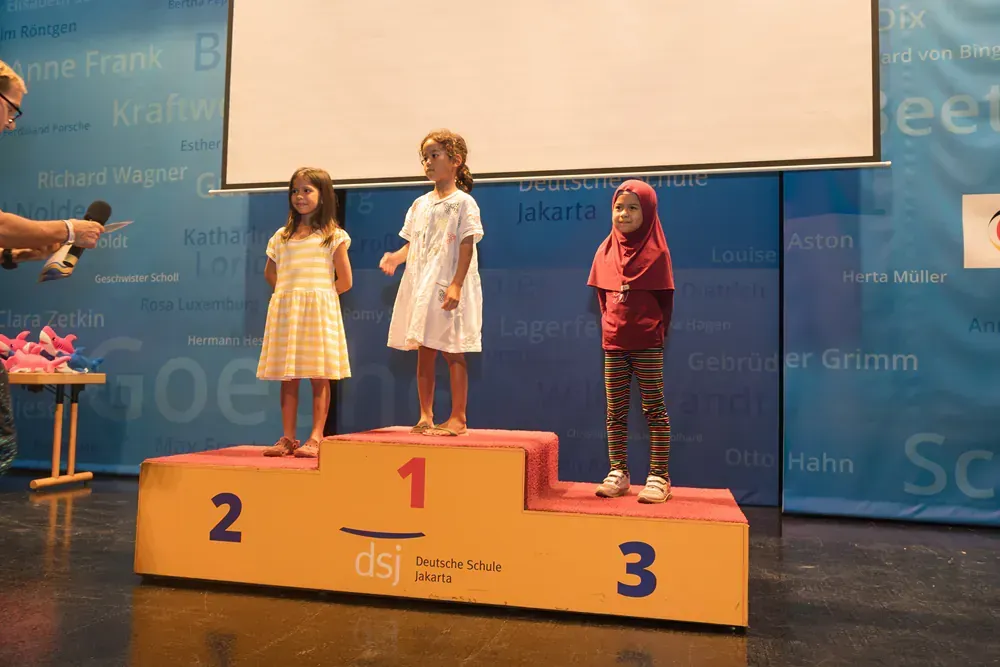 Three young girls stand on a podium with the number 1 2 and 3 on it