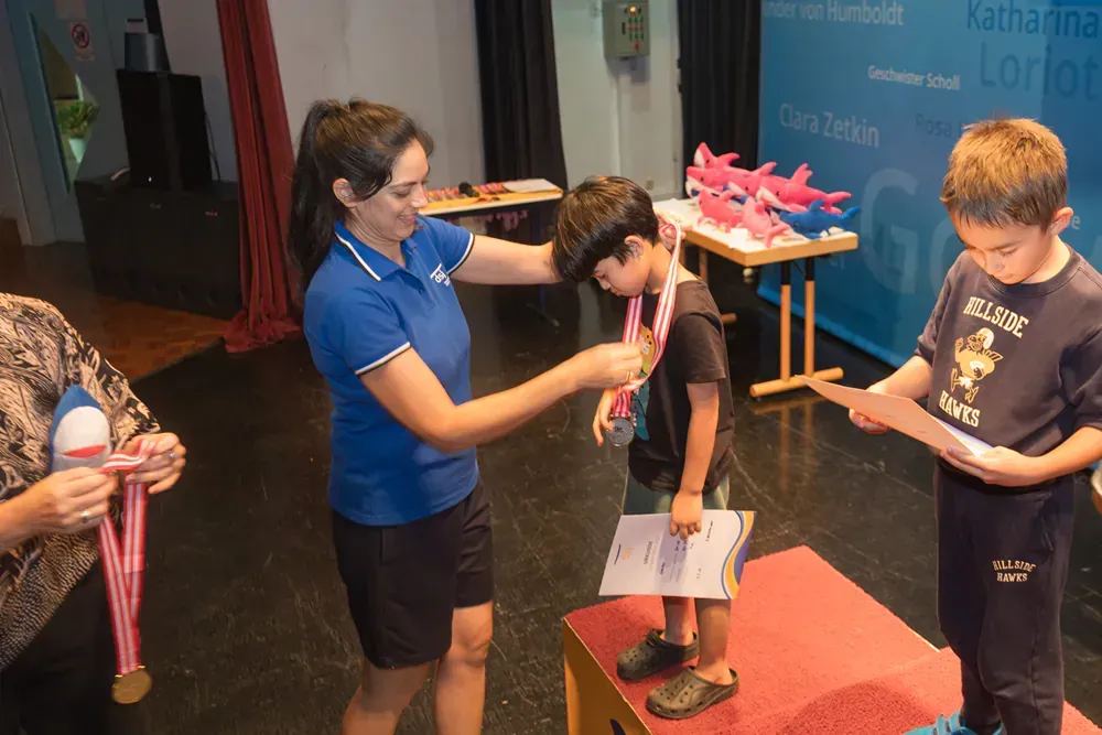A woman is putting a medal around a boy 's neck