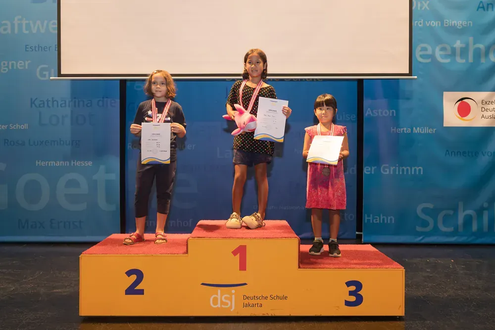 Three young girls are standing on a podium holding awards.
