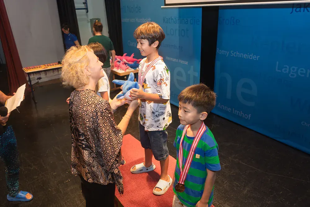 A woman is giving a medal to two young boys.