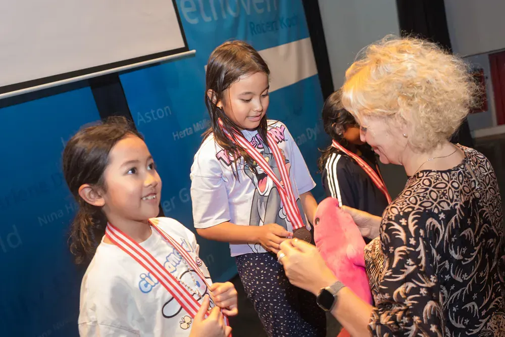 A woman is putting a medal on a little girl 's neck.