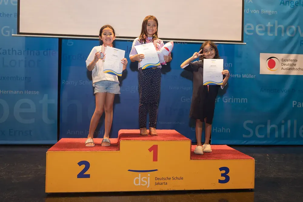 Three young girls are standing on a podium holding certificates.