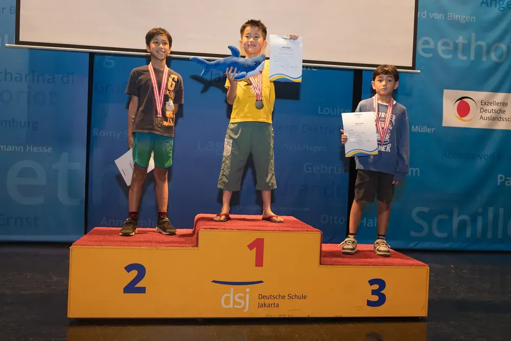 Three young boys are standing on a podium with the number 1 on it