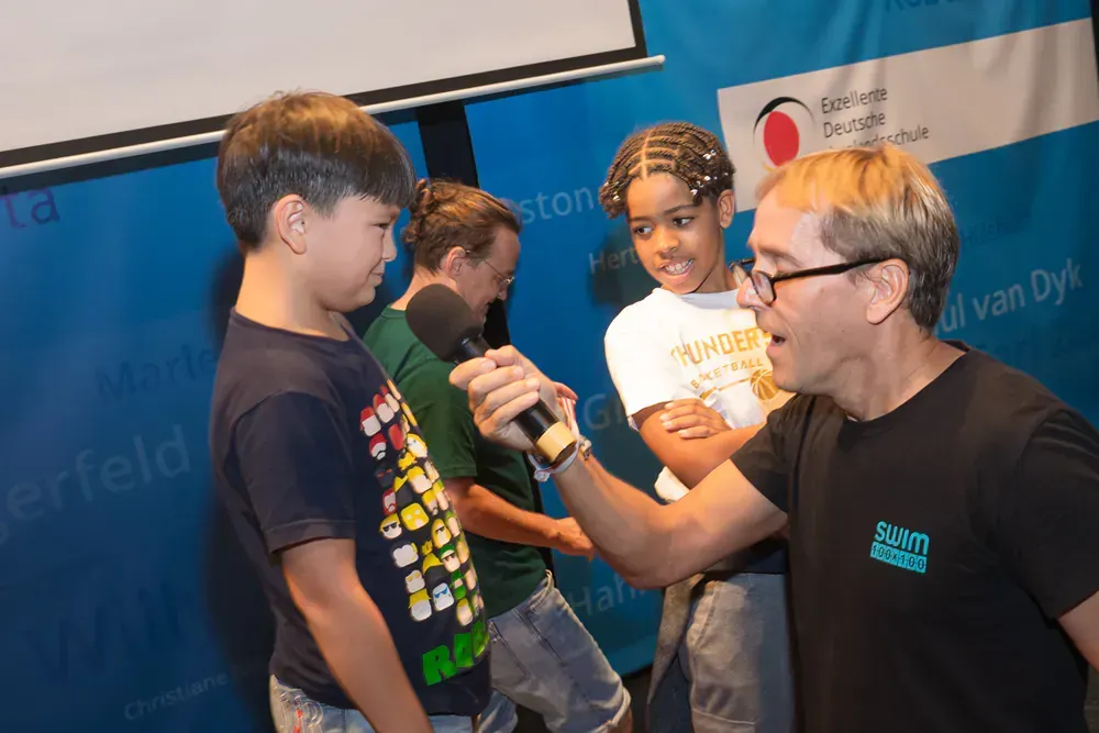 A man is holding a microphone in front of a group of children.