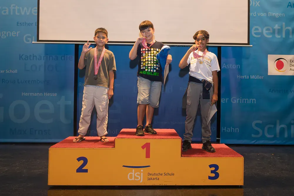 Three young boys are standing on a podium with medals around their necks