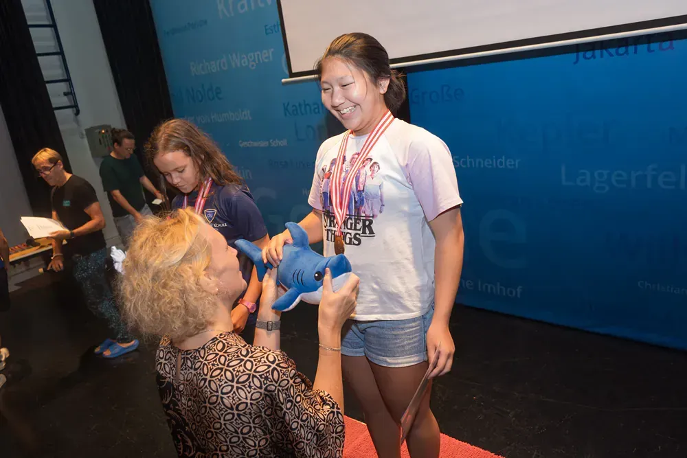 A woman is giving a medal to a young girl who is holding a stuffed dolphin.