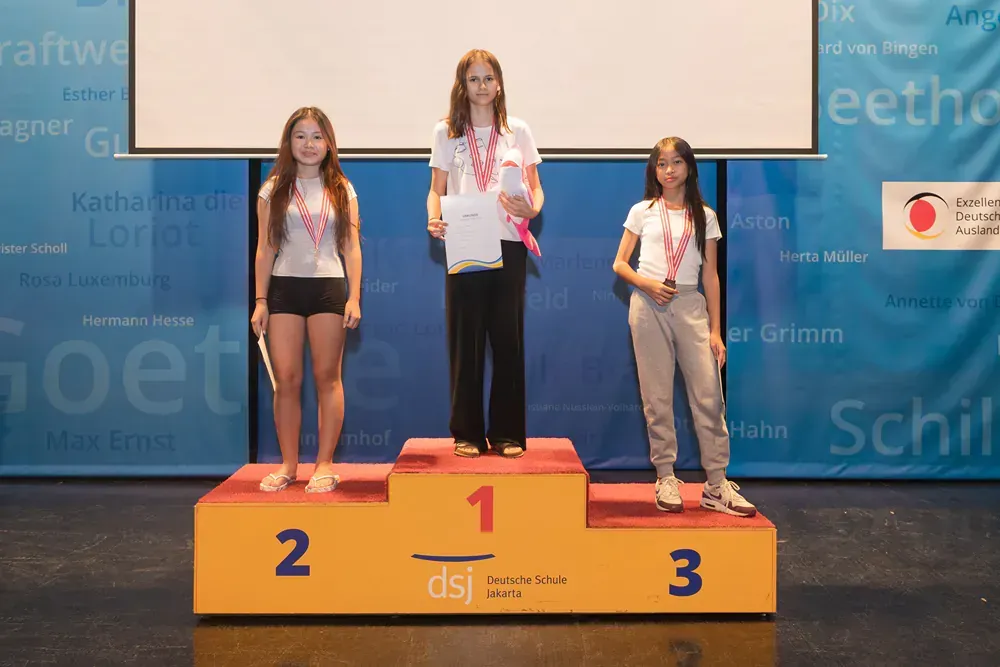Three girls are standing on a podium with the number 1 on it