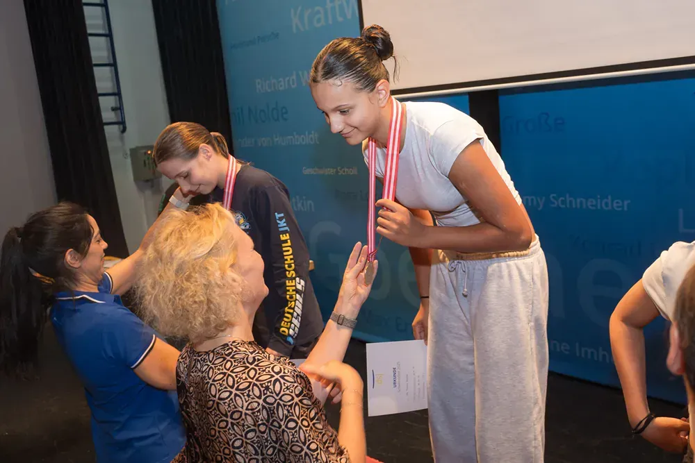A woman with a medal around her neck is being helped by another woman