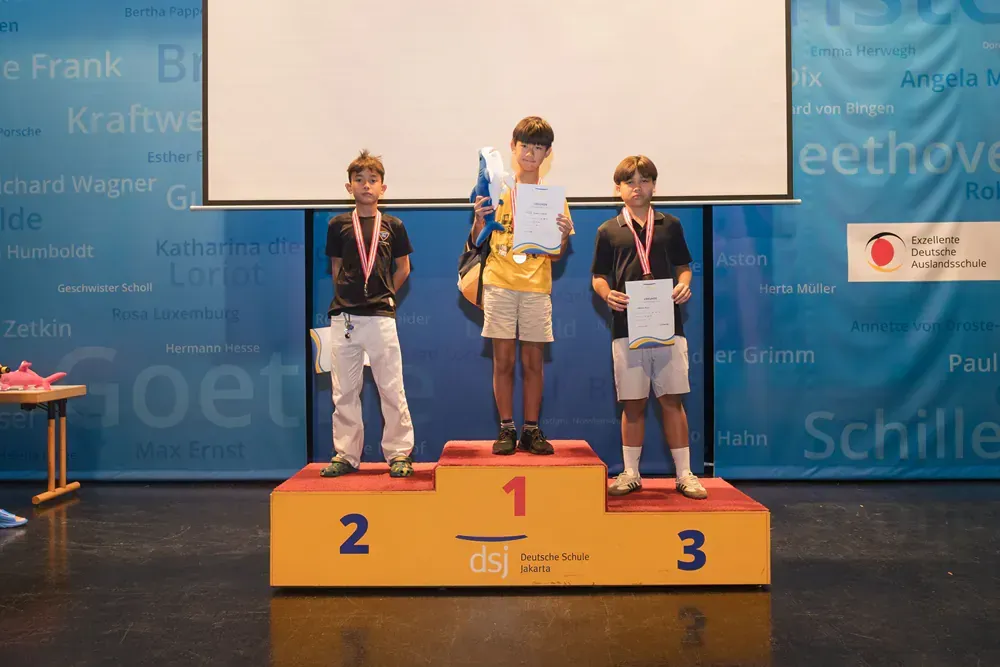 Three young men are standing on a podium holding awards.