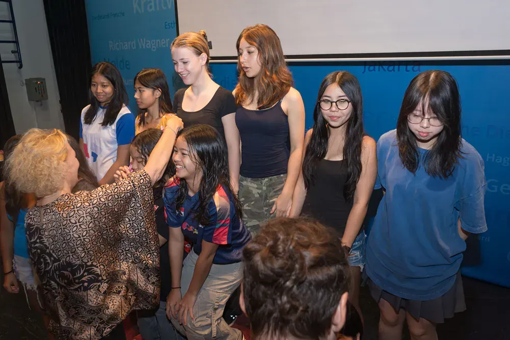 A group of young girls are standing around a woman in a room.