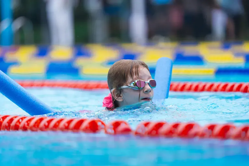 A young girl is swimming in a pool with foam noodles.