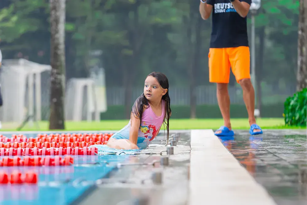 A little girl is laying on the edge of a swimming pool.