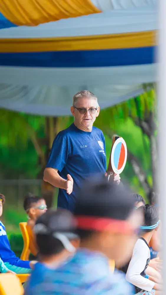 A man is standing in front of a group of people holding a tennis racket.