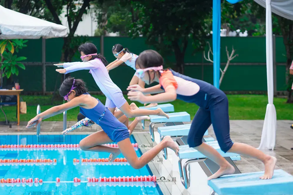 A group of young girls are jumping into a swimming pool.