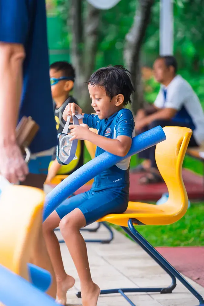 A young boy is sitting on a chair in a swimming pool.