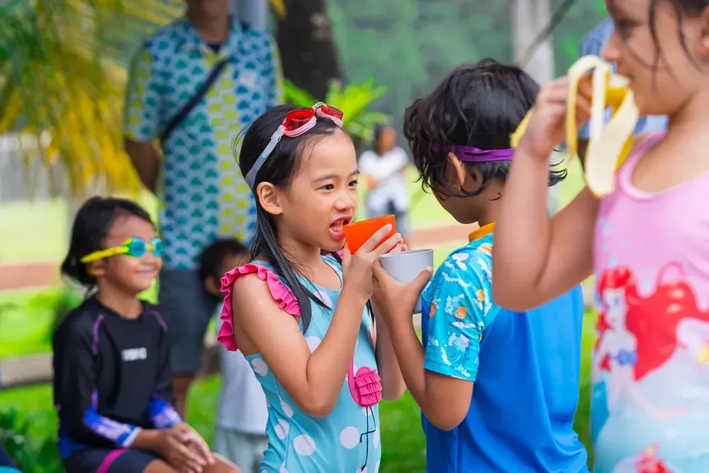 A group of children are playing with water balloons and a girl is drinking from a cup.
