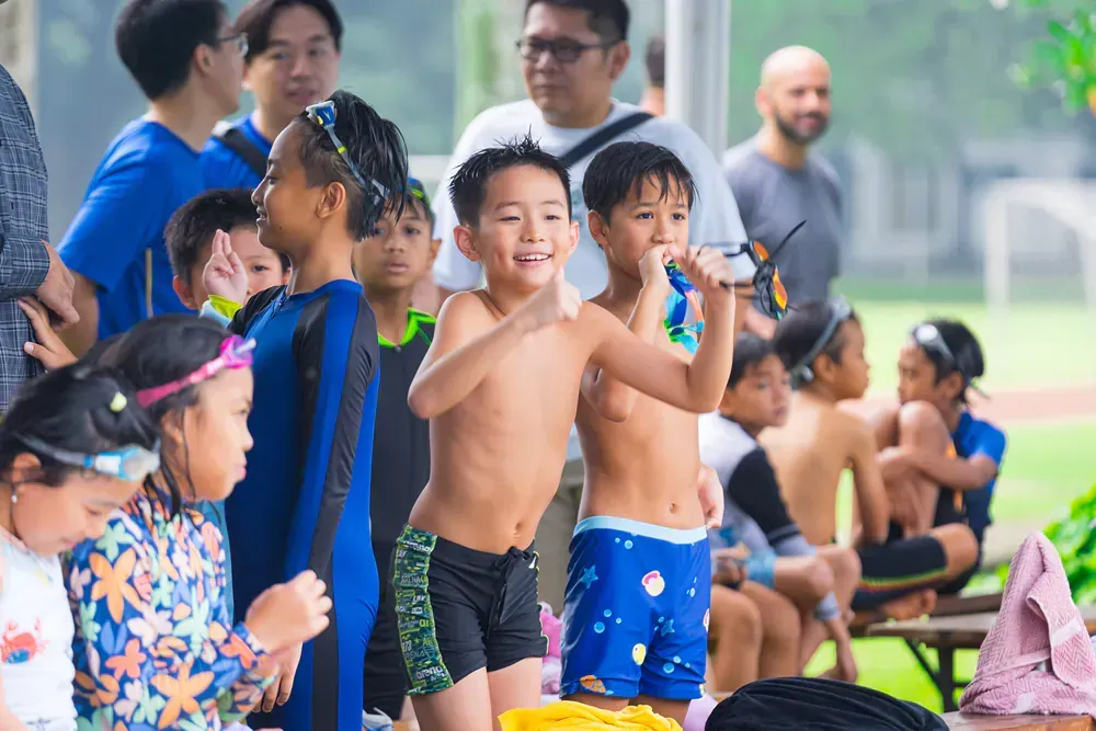 A group of children are sitting on a bench at a swimming pool.