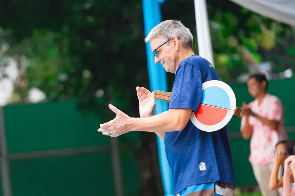A man wearing a blue shirt and sunglasses is holding a wooden propeller.