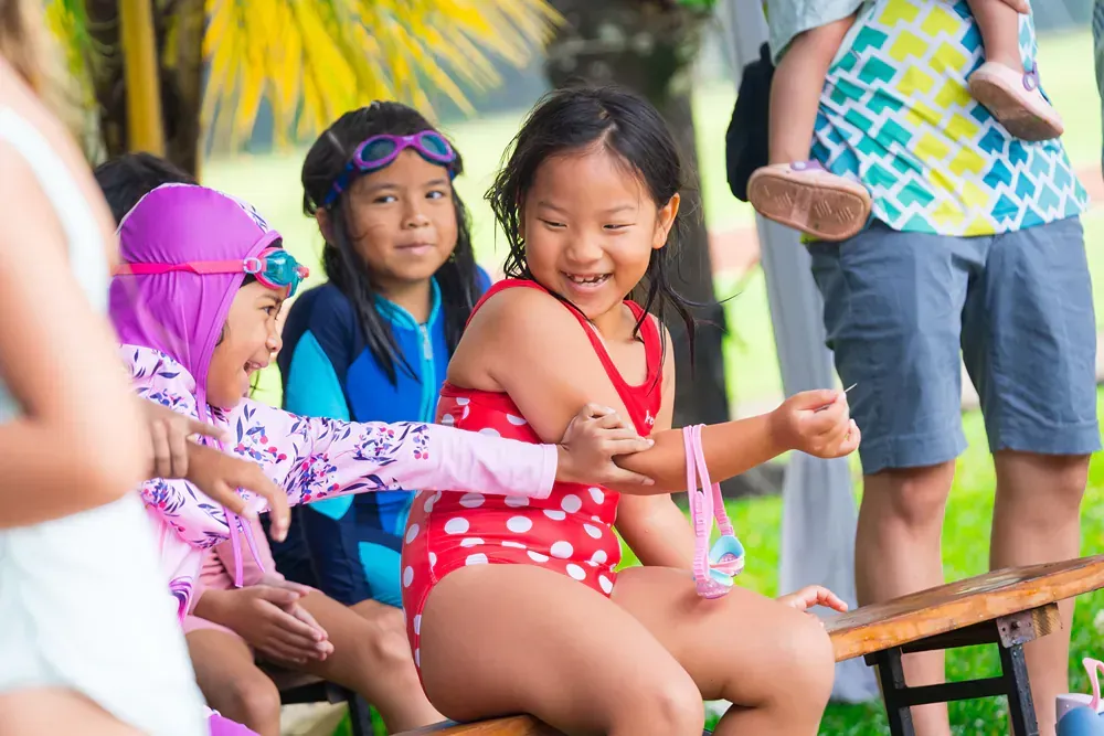 A group of young girls in swimsuits are sitting on a bench.