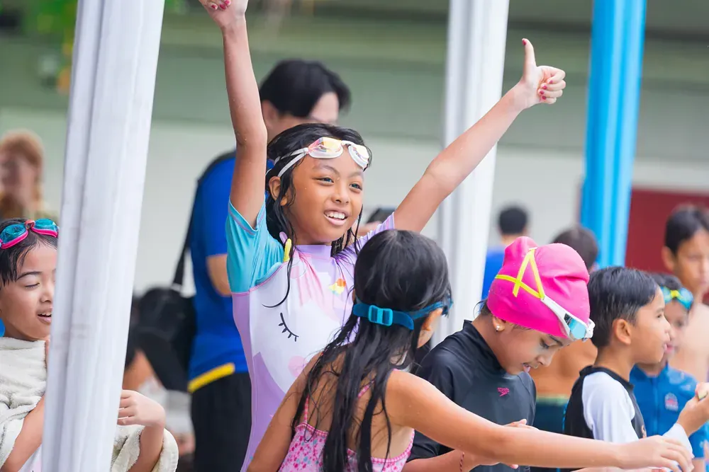 A group of children are standing around a pool giving a thumbs up.
