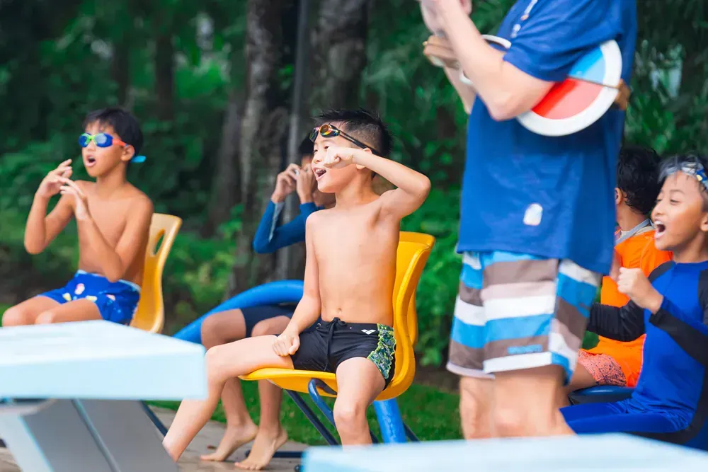 A group of young boys are sitting on a diving board at a swimming pool.