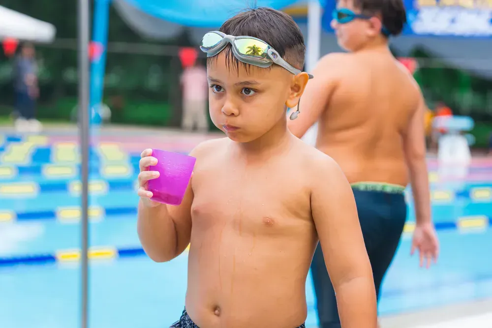 A young boy is holding a cup of water in front of a swimming pool.