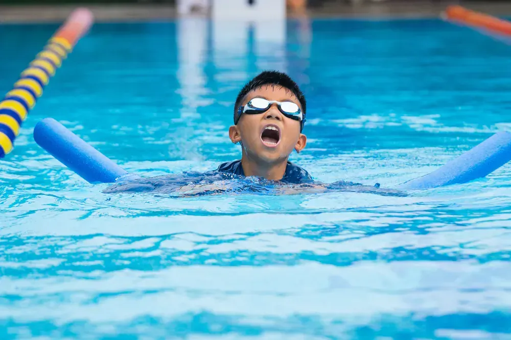 A young boy is swimming in a pool with foam noodles.
