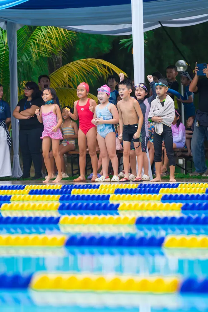 A group of children are standing on the edge of a swimming pool.