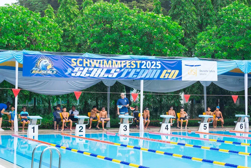 A man is standing in front of a swimming pool with a sign that says schwimmfest 2025.