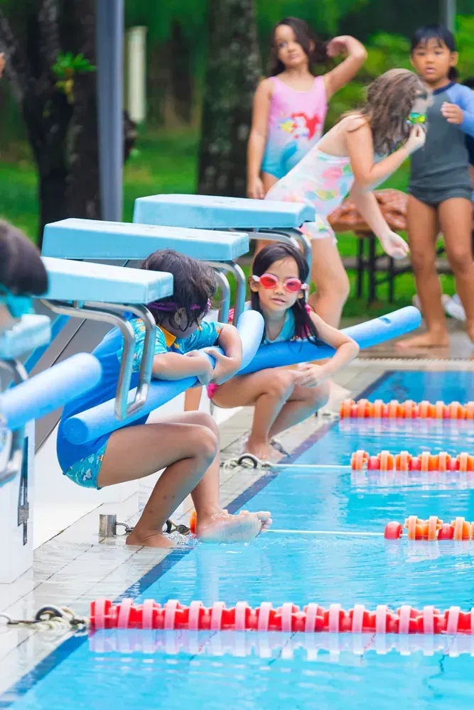 A group of young girls are sitting on the edge of a swimming pool.