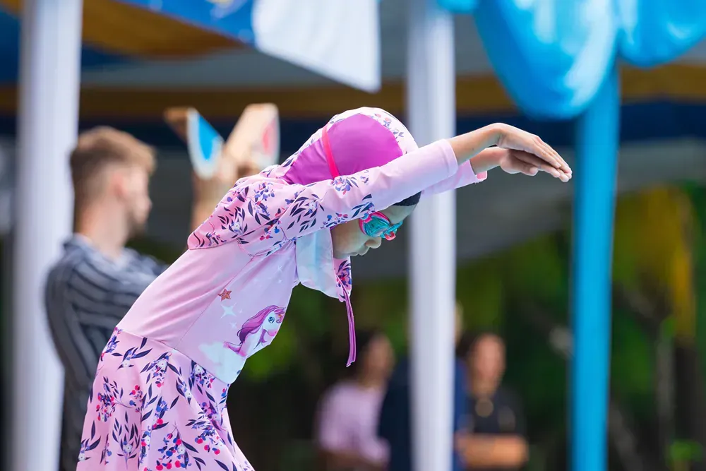 A little girl is wearing a pink swimsuit and a pink hat.