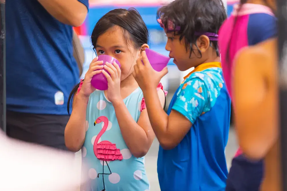 A boy and a girl are drinking from plastic cups.