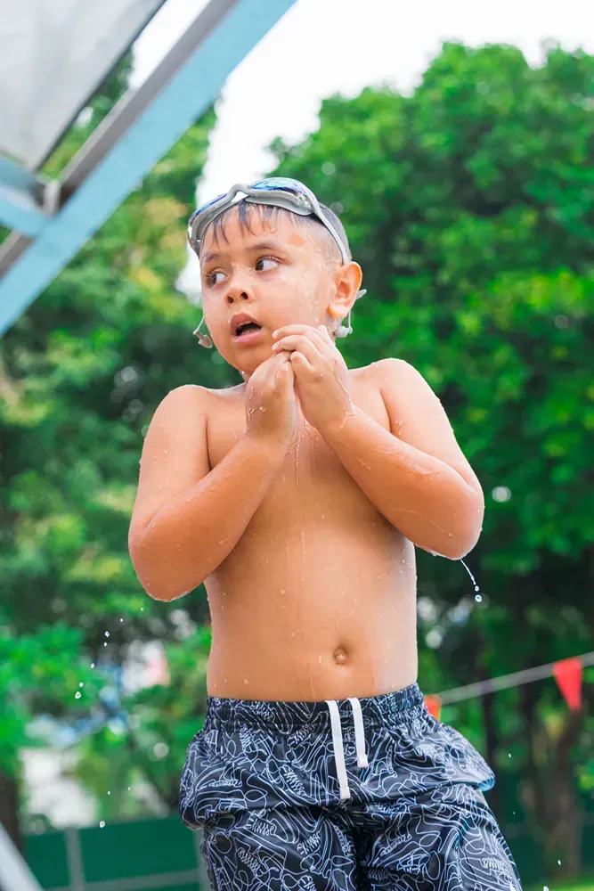 A young boy is standing in a swimming pool without a shirt on.