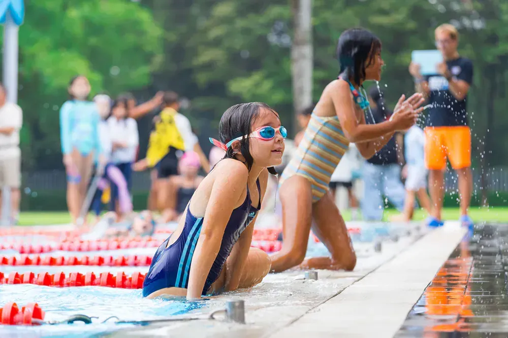 Two young girls are sitting on the edge of a swimming pool.