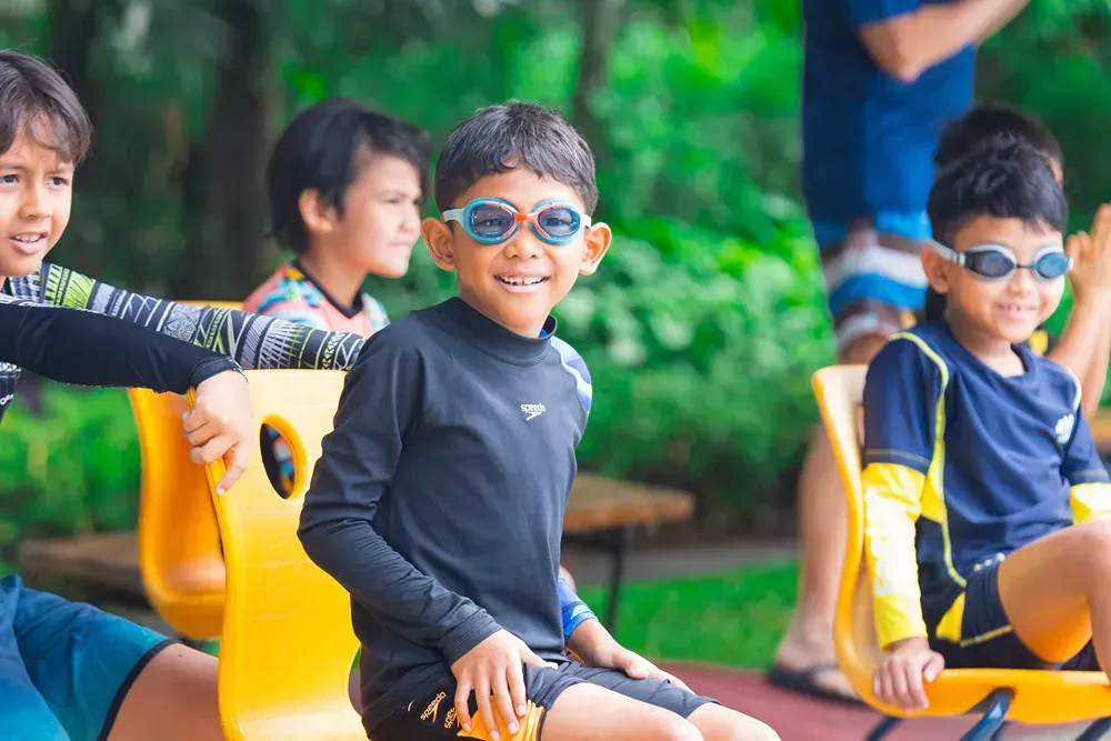 A group of young boys wearing swimming goggles are sitting in yellow chairs.