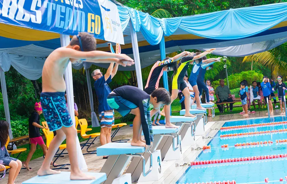 A group of young boys are getting ready to jump into a swimming pool.